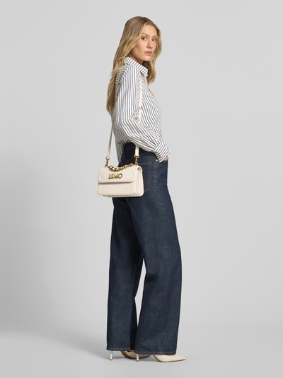 Frauenmodel trägt Handtasche mit Label-Applikation von Liu Jo White in Creme mit goldfarbenen Details, Ganzkörperansicht von vorne. Breite 23 cm, Länge 14 cm, Tiefe 8 cm, Schulterriemen 110 cm, Hauptfach mit Überschlag und Klickverschluss, Tragehenkel und Schulterriemen.
