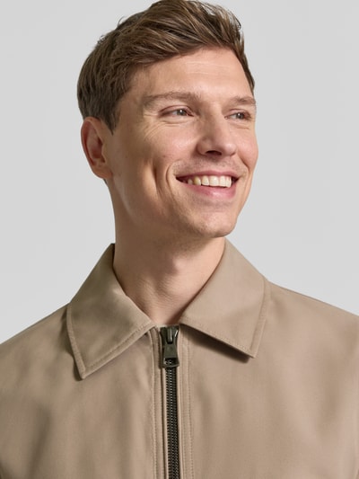 Męski model nosi Regular Fit Blouson mit Umlegekragen Modell 'LIGHT 2.0' od Strellson, gładki beżowy materiał, krój regular fit, zamek błyskawiczny, detal: kołnierz, zbliżenie na górną część ciała.