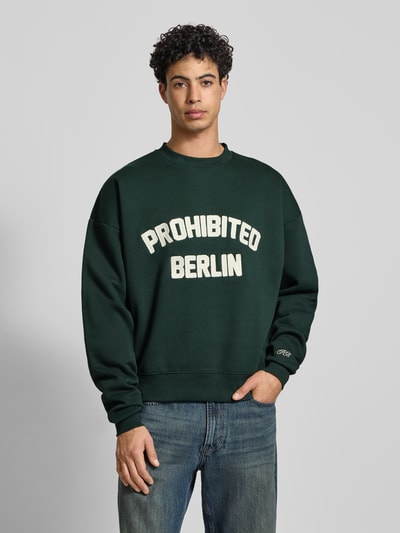 Männermodel trägt Oversized Sweatshirt mit Label-Detail von PROHIBITED, dunkelgrün, Baumwoll-Mix, gerippte Abschlüsse, Rundhalsausschnitt, Ganzkörperansicht von vorne.