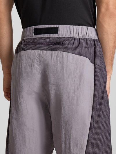 Mężczyzna nosi Shorts mit Logo und Gürtel von The North Face, krój regular fit, pasek, logo, elastyczny pas, szerokość w rozmiarze M 42 cm, długość wewnętrzna nogawki 24 cm, tekstura matowa i gładka, kontrastowe szarości, widok na całe plecy.