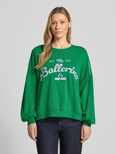 Frauenmodel trägt Oversized Sweatshirt aus Baumwoll-Mix Modell 'JAMIE' von Vero Moda in Grün mit Motiv-Print, Ganzkörperansicht von vorne.