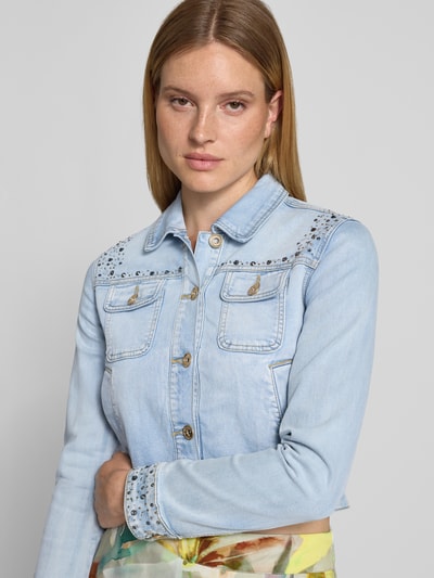 Frauenmodel trägt Cropped Jeansjacke mit Ziersteinbesatz von Betty Barclay, hellblau, Baumwoll-Mix mit Viskose-Anteil, Knopfleiste, Brusttaschen, Nahaufnahme Oberkörper. Rückenlänge bei Größe 36: 48 cm, Schulterbreite: 40 cm, Brustweite: 46 cm, Ärmellänge: 60 cm.