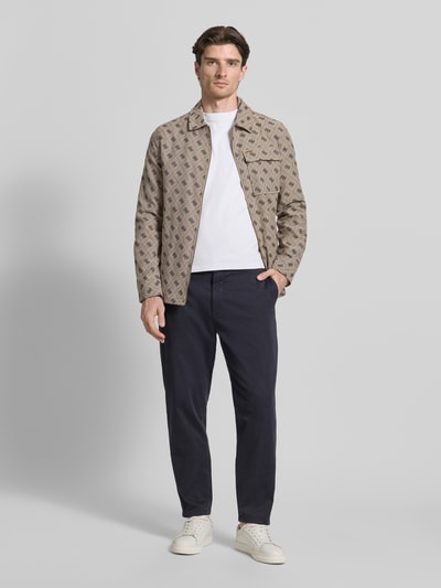 Männermodel trägt Regular Fit Jacke mit Brusttasche von Guess aus Baumwoll-Mix, Allover-Logo-Stitching, Reißverschluss, Ganzkörperansicht von vorne. Rückenlänge bei Größe M: 73 cm, Schulterbreite: 45 cm, Brustweite: 51 cm, Ärmellänge: 65 cm.