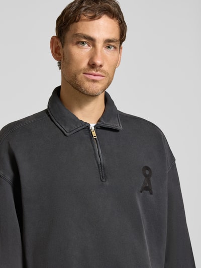 Mężczyznamodel nosi Relaxed Fit Troyer aus reiner Baumwolle Modell 'ICONIC' od ARMEDANGELS, ciemnoszary kolor, gładka tekstura, zamek, logo, zbliżenie górnej części ciała.