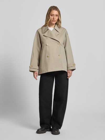 Frauenmodel trägt Trenchjacke mit Reverskragen Modell 'HEATHER' von G-LAB, Gerader-Schnitt, beige, Knopfverschluss, Ärmelriegel, Ganzkörperansicht von vorne. Kontext: Rückenlänge bei Größe S 70 cm, Schulterbreite 48 cm, Brustweite 52 cm, Ärmellänge 51 cm.