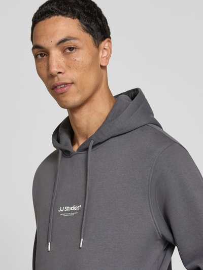 Männermodel trägt Regular Fit Hoodie aus Baumwoll-Mix Modell 'Soho' von JACK & JONES in Grau, sichtbarer Tunnelzug, Nahaufnahme Oberkörper.