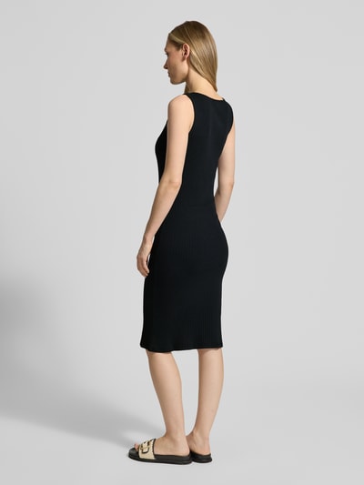 Männermodel trägt knielanges Kleid aus bawełniany-mix Modell 'RUBY' von Vero Moda, czarny, strukturalna faktura, krój slim fit, bez rękawów, prosty dół, całkowity widok z tyłu.
