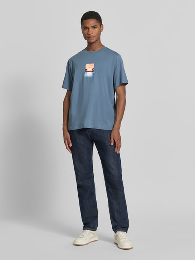 Mannenmodel draagt Regular Fit T-Shirt uit zuiver katoen model 'ASPEN' van SELECTED HOMME, effen blauw met motiefprint, jerseytextuur, korte mouw, ronde hals. Vooraanzicht volledige lichaamsopname.