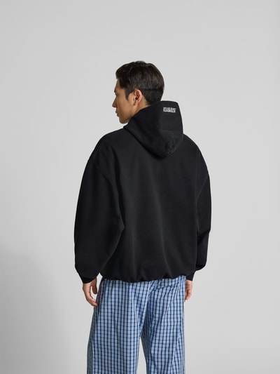 Männermodel trägt Oversized Sweatjacke aus Baumwolle von VETEMENTS in Schwarz mit Zweiwege-Reißverschluss, Känguru-Tasche und elastischen Abschlüssen, Herren Modell, Rückenlänge 75 cm, Schulterbreite 50 cm, Ärmellänge 78 cm, Ganzkörperansicht Rückansicht.