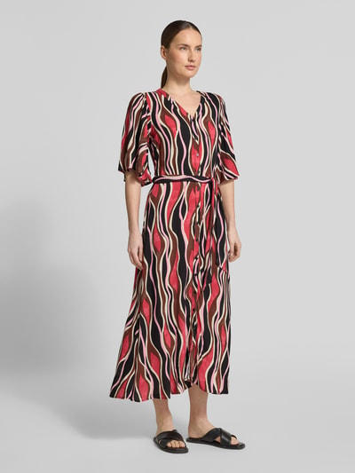 Vrouwenmodel draagt Regular Fit midi-jurk uit zuiver viscose model 'Cammi' van Soyaconcept in rood-zwart met patroon, halflange mouwen, V-hals, getailleerde pasvorm, afneembare stoffen band, doorlopende knoopsluiting, ruglengte maat S 124 cm, borstwijdte 50 cm, mouwlengte 37 cm, geheellichaamsaanzicht voorkant.