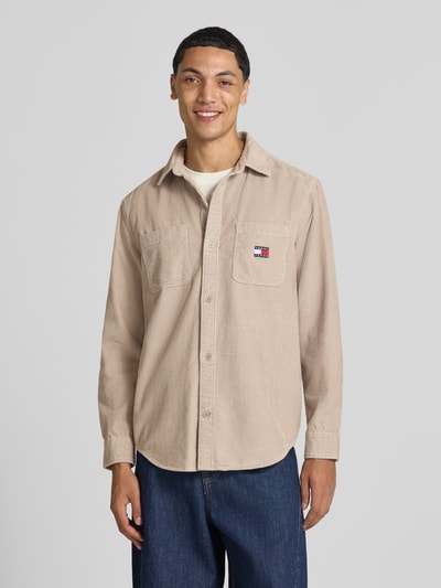 Männermodel trägt ein beiges Regular Fit Cordhemd mit Logo-Patch von Tommy Jeans, legere Struktur, Herren Freizeithemd, Ganzkörperansicht von vorne.
