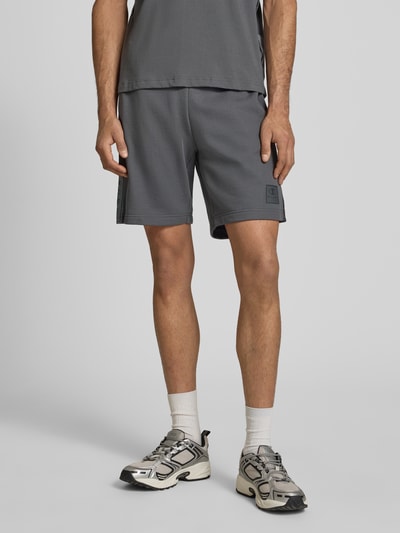 Männermodel trägt Shorts mit Logo und elastischem Bund von CHAMPION aus Baumwoll-Mix in Grau, Regular Fit, Nahaufnahme Unterkörper, Ganzkörperansicht von vorne.