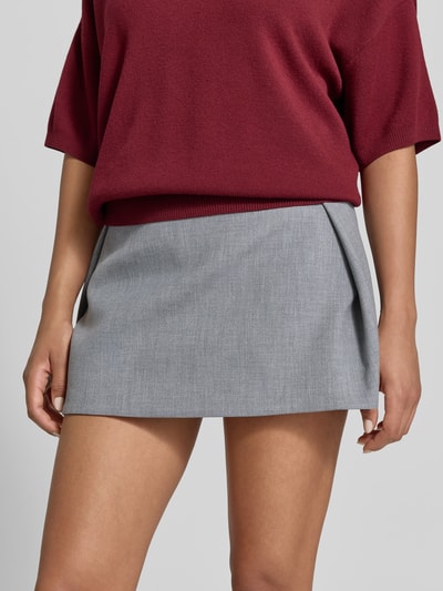 Frauenmodel trägt Minirock mit Viskose-Anteil von Iro in Grau mit Strukturmuster, ausgestellter Passform und gelegten Falten, Nahaufnahme Oberkörper. Elastischer Bund, elastischer Material-Mix.
