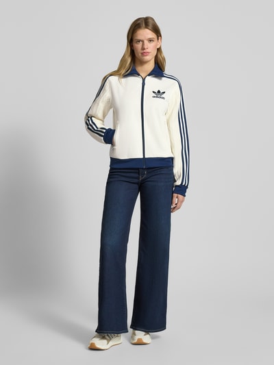 Frauenmodel trägt Strickjacke mit Reißverschluss von adidas Originals in Weiß und Blau, Baumwoll-Mix, lockerer Schnitt, Ganzkörperansicht von vorne.
