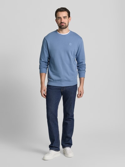 Męski model nosi Sweatshirt mit Label-Detail od Scotch & Soda, bawełna, luźny krój, ściągacze, okrągły dekolt, niebieski, widok całej sylwetki z przodu.