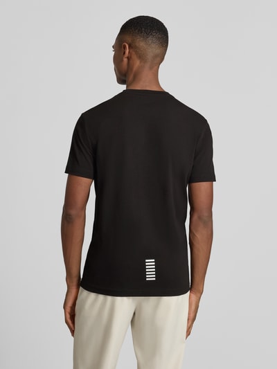 Männermodel trägt T-Shirt mit Label-Print von EA7 Emporio Armani in Schwarz, gerippter Rundhalsausschnitt, Ganzkörperansicht Rückansicht.
