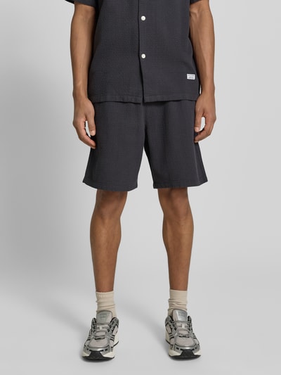 Männermodel trägt Regular Fit Sweatshorts aus reiner Baumwolle von Marc O'Polo Denim in Unifarben mit Label Patch, Piqué-Textur, Ganzkörperansicht von vorne.