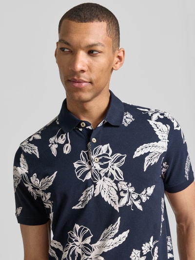 Mannelijk model draagt Modern Fit poloshirt met labeldetail van Lerros, donkerblauwe basis met wit bloemenpatroon, puur katoen, polokraag, korte knoopsluiting, ruglengte bij maat M 74 cm, nahaufnahme bovenlichaam.