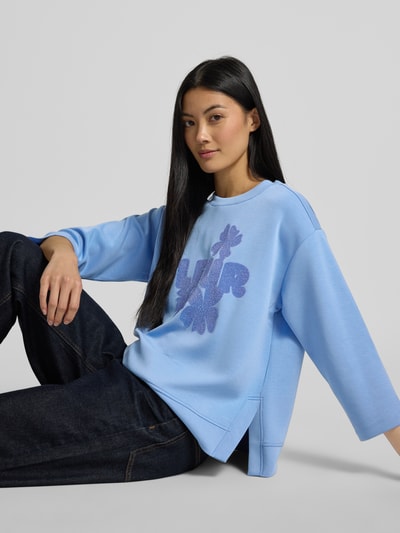 Kobiece modelka nosi Sweatshirt aus Modal-Mix mit 3/4-Arm od Milano Italy, niebieska bluza z nadrukiem, okrągły dekolt, krój relaxed fit, mieszanka modalu z dodatkiem streczu, Rękaw o dł. 3/4, widok całej sylwetki z przodu.