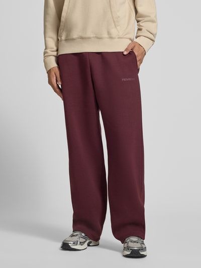 Männermodel trägt Straight Fit Sweatpants aus Baumwoll-Mix mit Label-Detail von REVIEW, burgunderrot, Eingrifftaschen, Nahaufnahme Unterkörper.