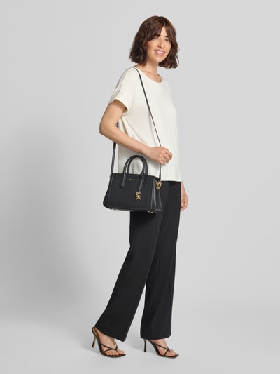 Frauenmodel trägt Handtasche aus Leder Modell 'LAILA' von MICHAEL Michael Kors mit Reißverschluss, Label-Applikation, Tragehenkel und Schulterriemen, schwarze Farbe, mittlere Größe, glatte Textur, Ganzkörperansicht von vorne.