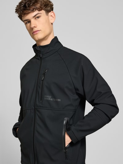 Männermodel trägt schwarze Softshell-Jacke mit Reißverschlusstaschen Modell 'ELITE' von HALO, Regular-Fit, Stehkragen, Label-Print, Nahaufnahme Oberkörper. Rückenlänge bei Größe M: 71 cm, Schulterbreite: 55 cm, Brustweite: 60 cm, Ärmellänge: 63 cm.