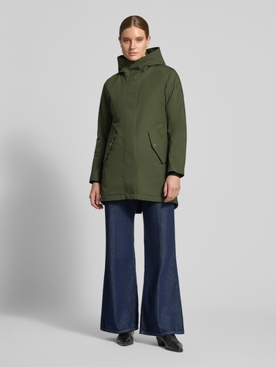 Frauenmodel trägt Regular Fit Parka mit Kapuze Modell 'Alana' von Didriksons in Olivgrün, strukturierte Oberfläche, Ganzkörperansicht von vorne. Rückenlänge 90 cm, Schulterbreite 38 cm, Brustweite 48 cm, Ärmellänge 74 cm.