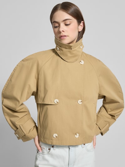 Vrouwenmodel draagt korte, lichtbeige trenchcoat van puur katoen met mouwsluitingen, dubbele knopen, platte kraag, regular fit, model 'MIA' van Topshop, geheel vooraanzicht