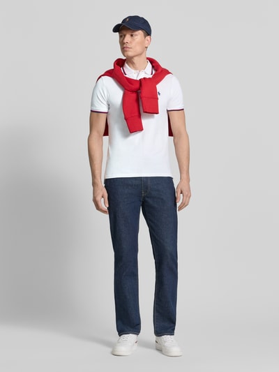 Männermodel trägt Slim Fit Poloshirt aus reiner Baumwolle von Polo Ralph Lauren, Optik: Unifarben, Regular-Fit, Logo-Stitching, Kontraststreifen, Polokragen, Kurzarm, gerippter Ärmelabschluss, Rumpfabschluss mit Seitenschlitzen, Materialverarbeitung: Piqué, Ganzkörperansicht von vorne.