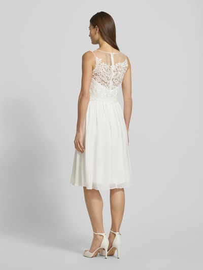 Kobiece modelka nosi Brautkleid mit floraler Spitze od Mascara, taliowany fason, szerokie ramiączka, półprzezroczysty materiał wierzchni, halka pod sukienkę, zapięcie na haftkę i wszyty zamek, biały kolor, widoczna szerokość klatki piersiowej 40 cm i długość tyłu 107 cm, kwiatowy wzór z koronki, całkowity widok sylwetki od tyłu.