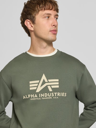 Männermodel trägt Regular Fit Sweatshirt aus Baumwoll-Mix mit Logo-Print von Alpha Industries in Oliv mit Rundhalsausschnitt, Nahaufnahme Oberkörper.
