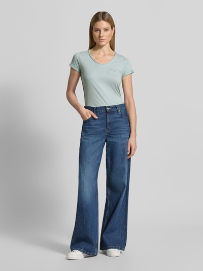 Modelka kobieca nosi damski t-shirt z brustaszą, krój regular fit, dekolt w serek, model 'GS23' od G.I.G.A. DX z bawełny, długość tyłu 64 cm w rozmiarze 36, jasny odcień, gładka tekstura, widok całej sylwetki z przodu.
