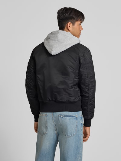 Männermodel trägt Jacke mit Reißverschlusstasche am Ärmel von Alpha Industries in Schwarz und Grau, Regular Fit, Ganzkörperansicht Rückansicht.