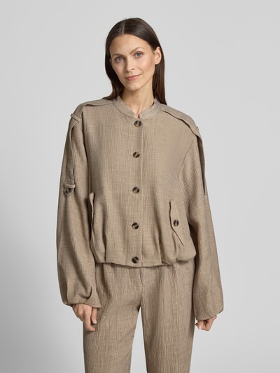 Kobiece modelka ma na sobie kurtkę z mieszanki wiskozy ze stójką model 'RINA' od YAS, krój relaxed fit, tkanina beżowa, listwa guzikowa, wpuszczane kieszenie z zapięciem na guzik, długość tyłu w rozmiarze 36: 54 cm, szerokość ramion w rozmiarze 36: 48 cm, szerokość w klatce piersiowej w rozmiarze 36: 57 cm, długość rękawów w rozmiarze 36: 61 cm, widok całościowy z przodu