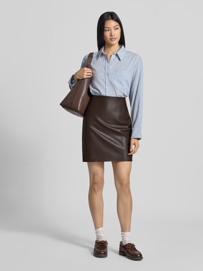 Frauenmodel trägt Minirock in Leder-Optik Modell 'DAGMAR' von VILA, körpernahe Passform, braun, glatte Textur, Ganzkörperansicht von vorne.