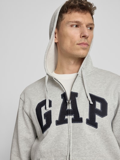 Männermodel trägt Sweatjacke mit Logo und Känguru-Tasche von GAP in Hellgrau, Baumwoll-Mix, Regular-Fit, Nahaufnahme Oberkörper.