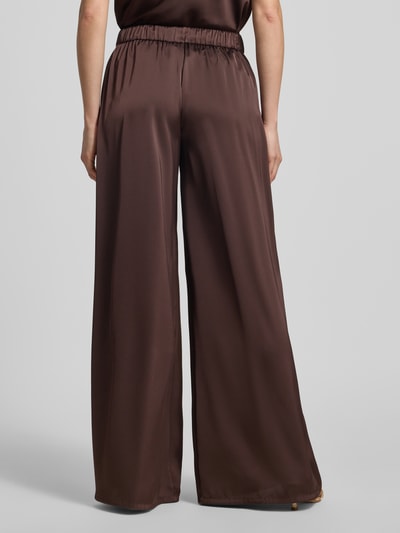 Modelka nosi Stoffhose mit elastischem Bund od V by Vera Mont, satynowy materiał, kolor brązowy, szeroka nogawka, relaxed fit, szerokość w rozmiarze 36: 28 cm, długość nogawki wewnętrznej: 79 cm, widok całościowy z tyłu.
