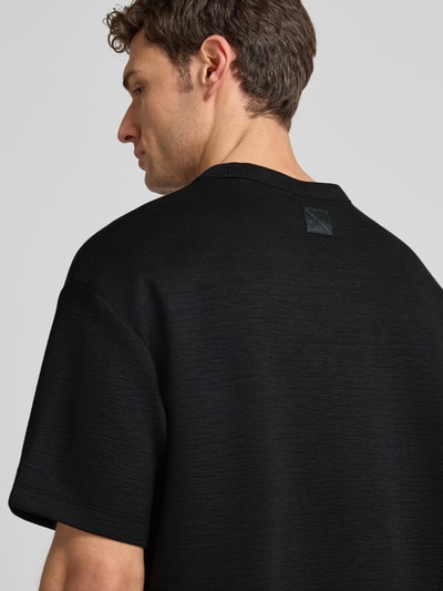 Männermodel trägt T-Shirt mit Rundhalsausschnitt Modell 'CRINKLE CREPE SPACER' von CK Calvin Klein in Schwarz mit Strukturmuster, Nahaufnahme Rückansicht.