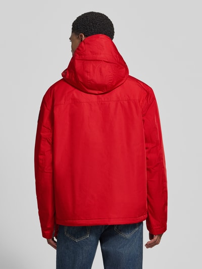 Männermodel trägt Jacke mit Kapuze und kurzem Reißverschluss von Napapijri in Rot, Rückansicht, Ganzkörperansicht Rückansicht. Modell RAINFOREST NEXT, gerader Schnitt, Kapuze mit Tunnelzug und Kordelstoppern, Pattentasche, Label-Patches, glatte Textur.