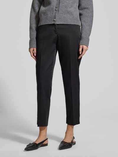 Kobiece modelka nosi czarne spodnie materiałowe Straight Fit Stoffhose mit Lyocell-Anteil Modell 'Mara' od Brax, z bawełnianą mieszanką z dodatkiem lyocellu, zaprasowane na kant, skrócony fason, kieszenie boczne i tylne, zapięcie na guzik i zamek, szerokość w rozmiarze 36: 39 cm, długość nogawki wewnętrznej w rozmiarze 36: 68 cm; widok całej sylwetki z przodu.