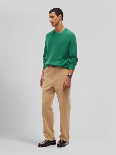 Mannenmodel draagt Regular Fit Pullover uit pure katoen van Tommy Hilfiger in groen, gecombineerd met beige broek, volledig lichaamsbeeld van voren.