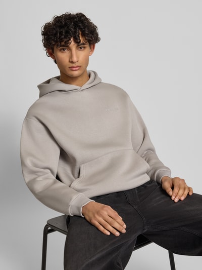 Männermodel trägt Hoodie mit Känguru-Tasche von REVIEW in Hellgrau, lockere Passform, elastische Abschlüsse, Nahaufnahme Oberkörper.
