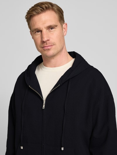 Männermodel trägt Relaxed Fit Sweatjacke aus reiner Baumwolle Modell 'Hootailored262X' von HUGO in Unifarben, Nahaufnahme Oberkörper.