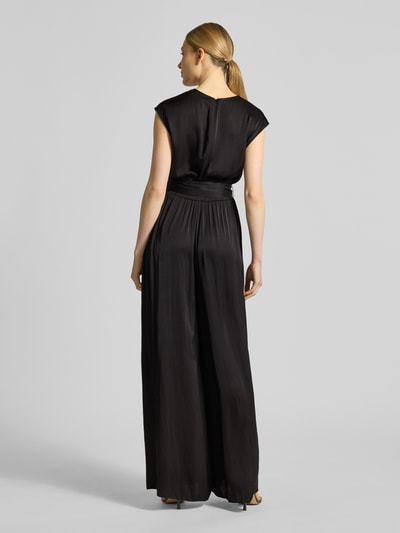 Modelka damska ma na sobie Regular Fit Jumpsuit mit Taillengürtel zum Binden von s.Oliver RED LABEL, efekt: jednolity kolor, krój regular fit, dekolt w serek, zapięcie: zamek błyskawiczny, bez rękawów, wpuszczane kieszenie, wykończenie materiału: satyna; kolor czarny, całość z delikatnym połyskiem, gładka faktura. Widok całej sylwetki z tyłu.