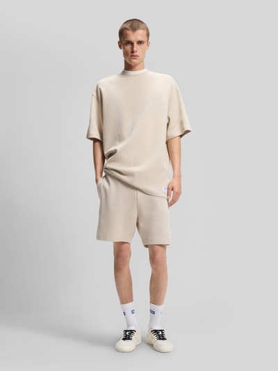 Männermodel trägt Relaxed Fit T-Shirt aus Baumwoll-Mix Modell 'NUWAFFLE' von HUGO in Optik: Unifarben mit Struktur-Muster, Label-Stitching-Applikation, Rundhals-Ausschnitt und Ärmelform: Kurzarm, Material: Baumwolle-Mix, helle Cremefarbe, Ganzkörperansicht von vorne.