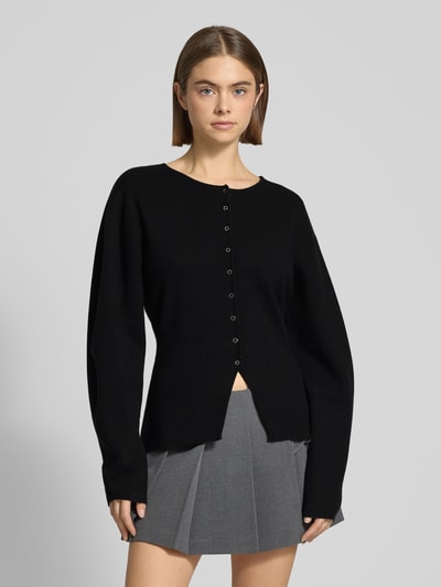 Frauenmodel trägt Regular Fit Strickjacke aus Viskose-Mix in Strick-Optik von Gina Tricot, schwarz, Rundhalsausschnitt, grauer Rock, Ganzkörperansicht von vorne.
