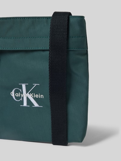 Produktfoto, Crossbody Bag mit Label-Stitching von CK Calvin Klein in Dunkelgrün mit schwarzem Schulterriemen und sichtbarem Reißverschluss, dezente Textur, Maße 21x21x3 cm, Hauptfach und Label-Stitching erkennbar