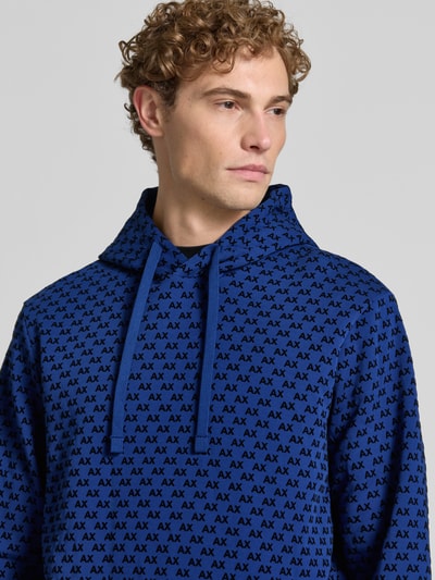 Männermodel trägt Regular Fit Hoodie aus Baumwoll-Mix von Armani Exchange in Blau mit Allover-Logo-Print, Nahaufnahme Oberkörper.