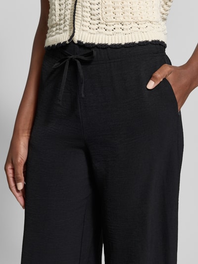Frauenmodel trägt Stoffhose mit Strukturmuster von Christian Berg Woman in Schwarz mit Tunnelzug und Eingrifftaschen, Nahaufnahme Oberkörper. Bundweite bei Größe 36: 38 cm, Innenbeinlänge bei Größe 36: 78 cm.