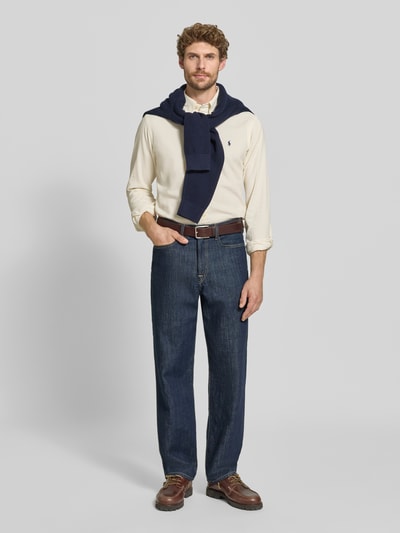Männermodel trägt Custom Fit Freizeithemd aus reiner Baumwolle von Polo Ralph Lauren in Creme, kombiniert mit blauer Jeans und braunen Schuhen, Ganzkörperansicht von vorne. Herren Freizeithemd von Polo Ralph Lauren.